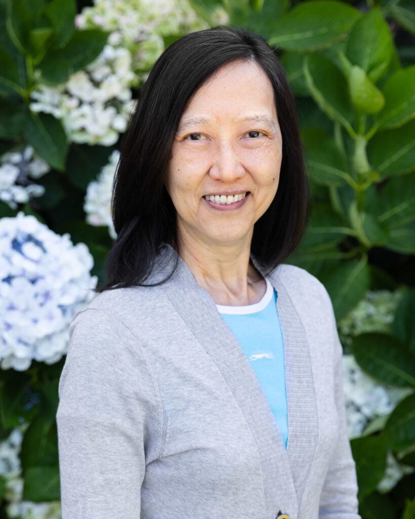 Smiling woman in garden with hydrangeas in background.