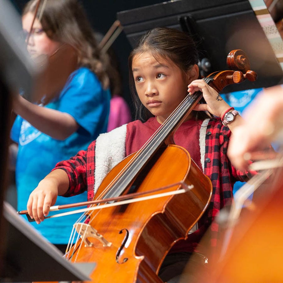 Young girl playing cello in orchestra.