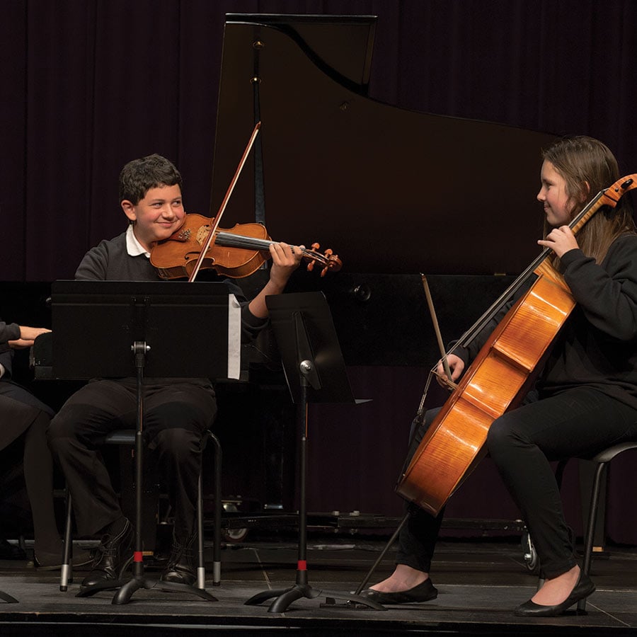Students playing violin and cello on stage.