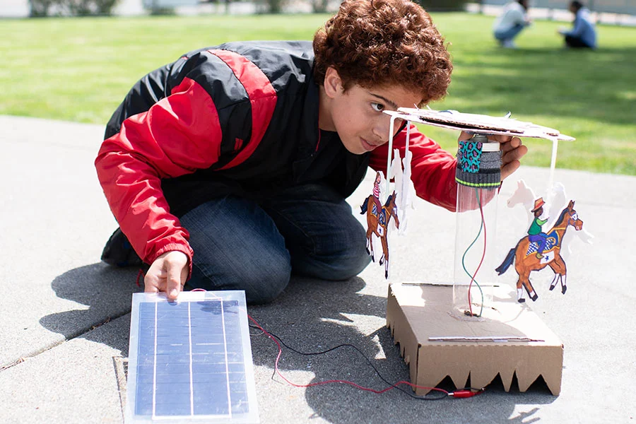 Child builds solar-powered motorized toy carousel outdoors.