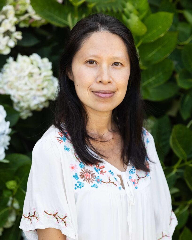 Person in embroidered blouse, greenery background.