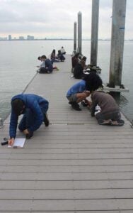 Students writing on dock by water.