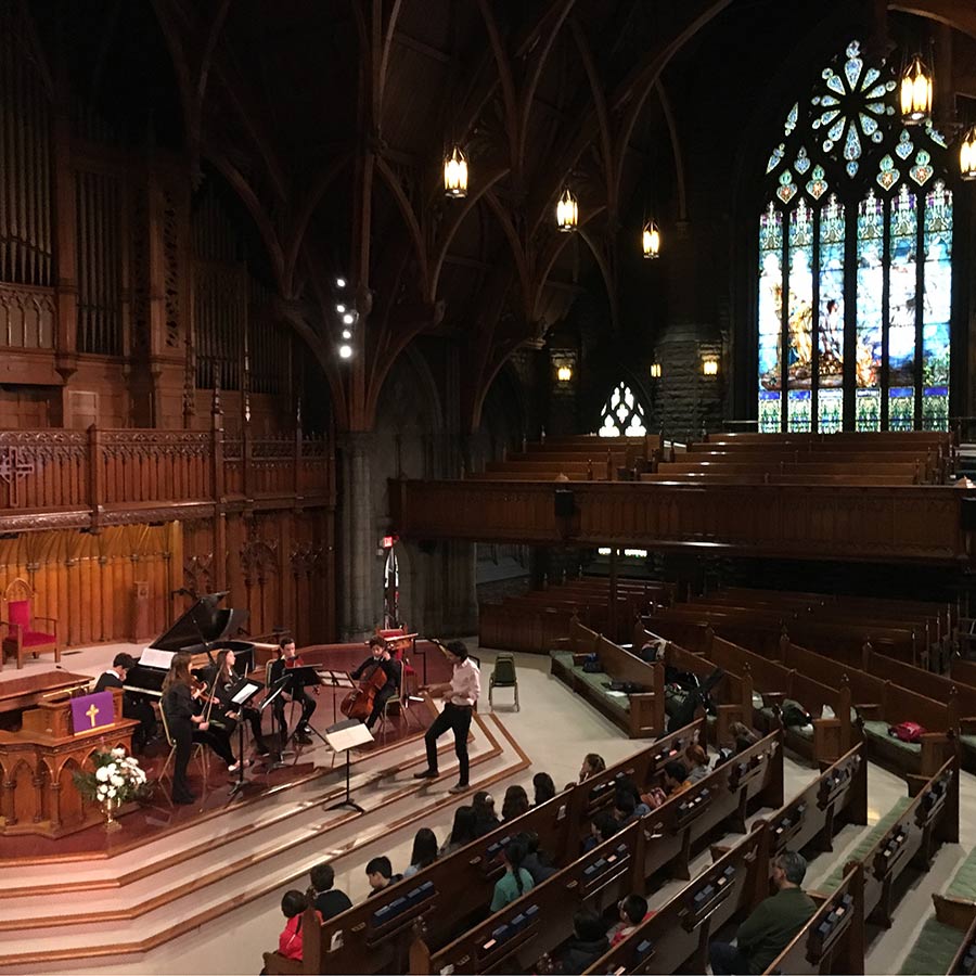 Musicians performing in a large church with stained glass.