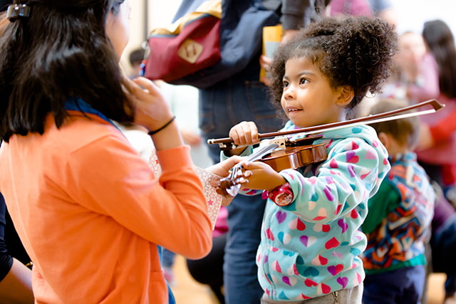 Child learning violin with teacher in classroom