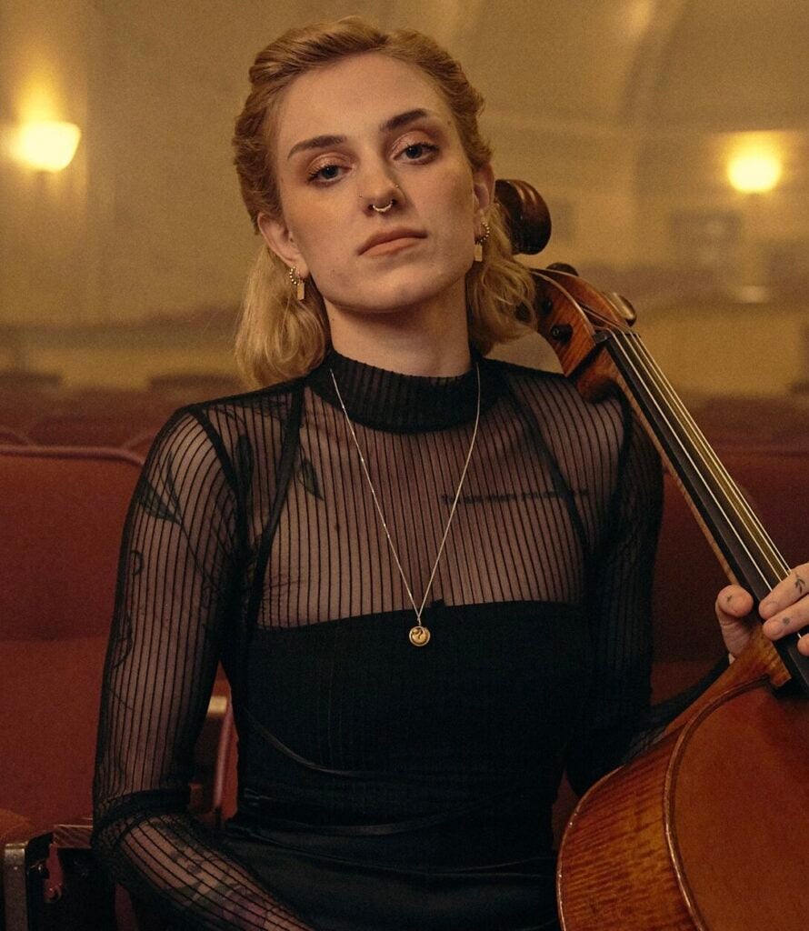 Musician holding a cello in a dimly lit room.