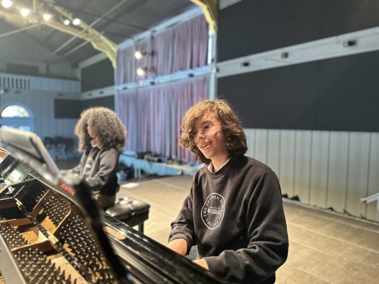 Two people playing piano on a stage.