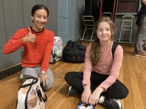 Two girls sitting on a wooden floor, smiling.