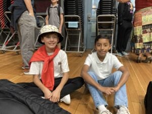 Two boys sitting on gym floor smiling.
