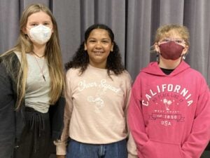 Three girls smiling, wearing casual clothes, and masks.