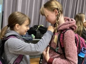 Two girls in school with backpacks, smiling.