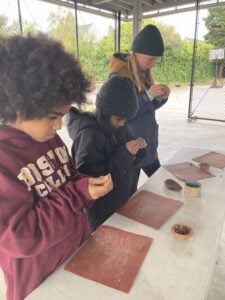 Children crafting clay pieces outdoors under shelter.