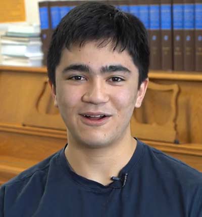Smiling person in library setting, wearing a microphone.