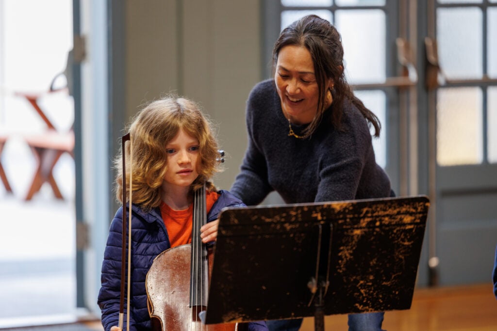 Teacher assisting child with cello practice.
