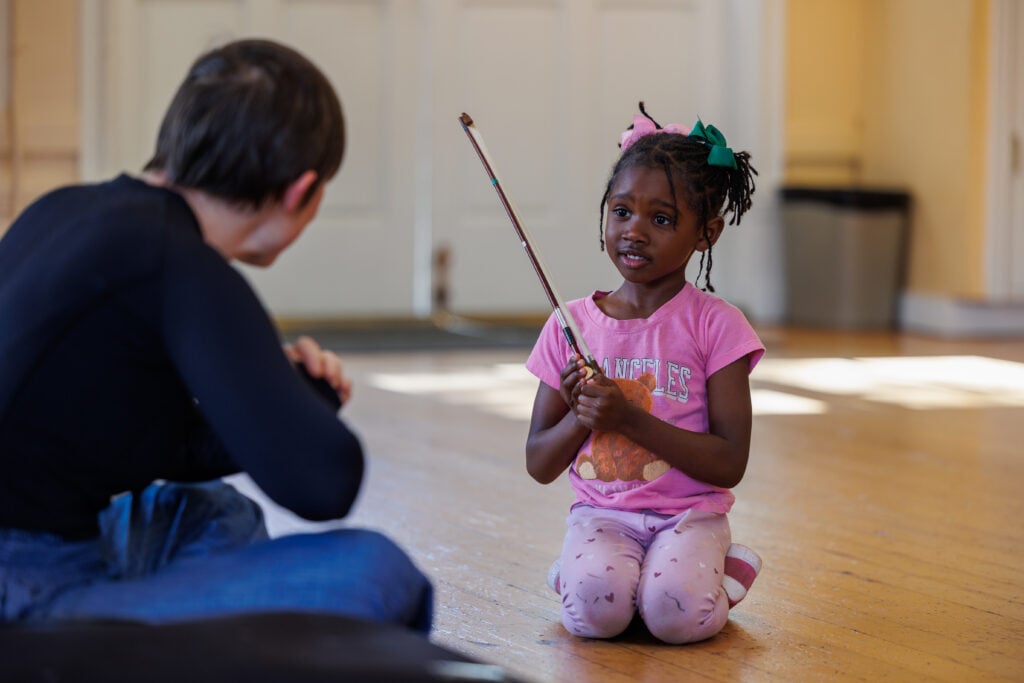 Child with a violin bow in a classroom.