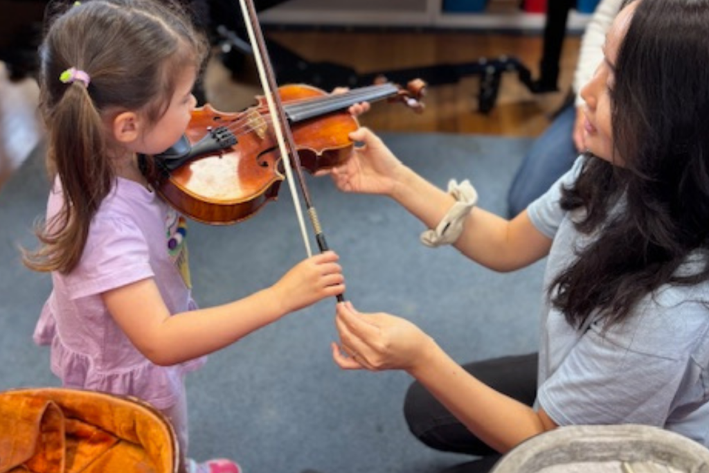 Child practicing violin with teacher guidance