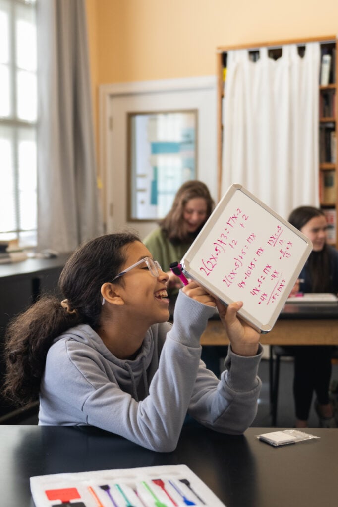 Girl writes math equations on small whiteboard
